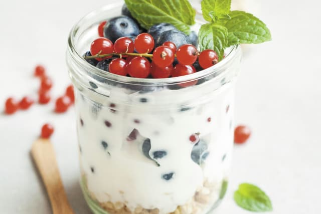 A breakfast jar containing berries, yogurt, oats, and more